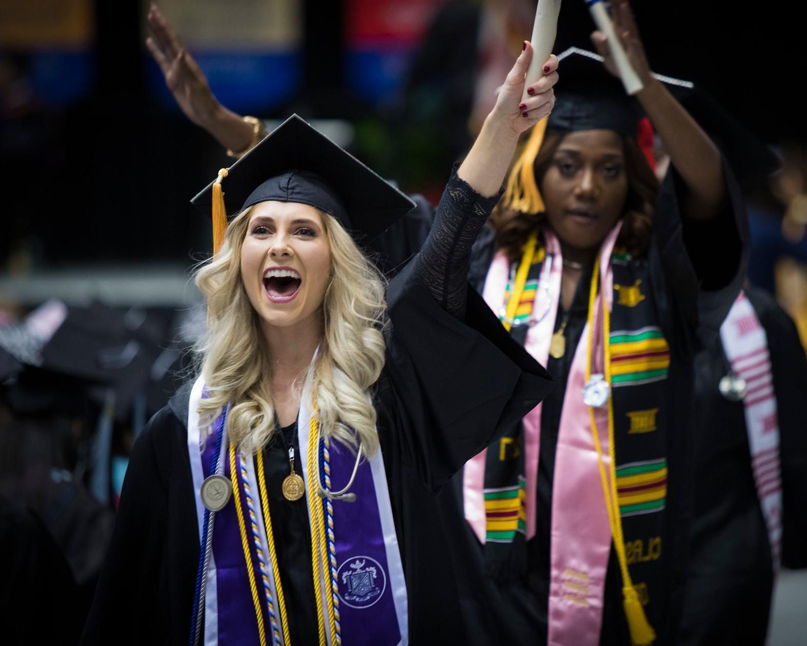 two women (one White and one African-American) walking with their diplomas